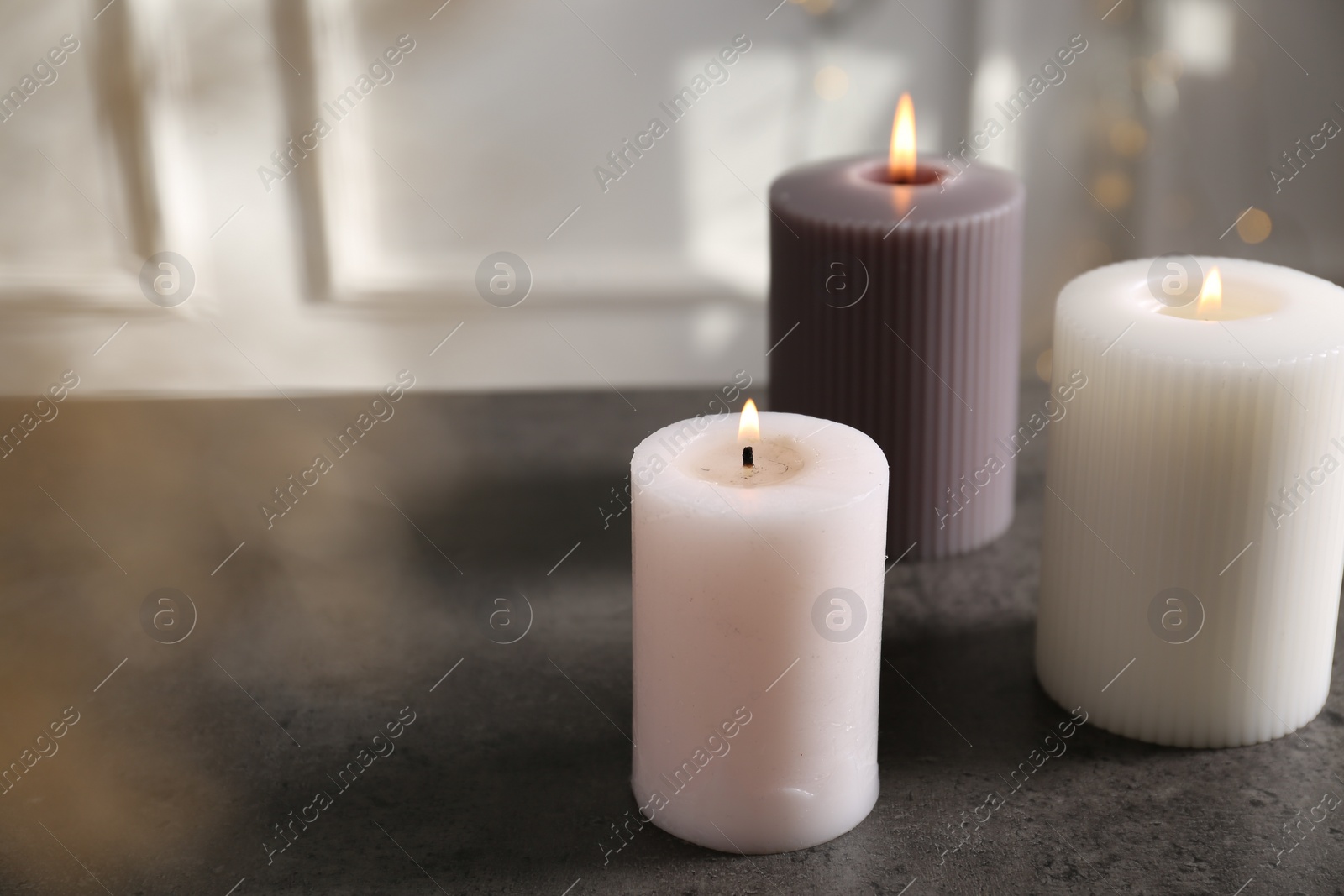Photo of Different burning candles on grey table indoors. Space for text
