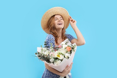 Beautiful woman in straw hat with bouquet of flowers on light blue background