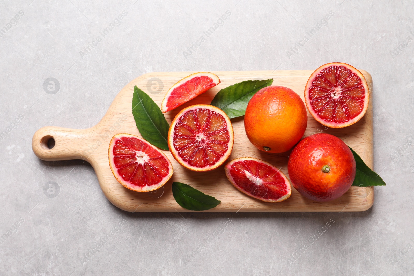 Photo of Ripe red oranges, green leaves and wooden board on light table, top view