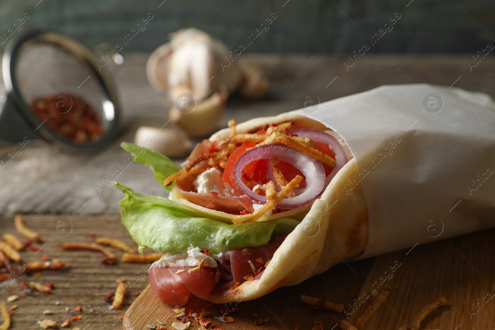 Photo of Delicious pita wrap with prosciutto and vegetables on wooden table, closeup. Space for text