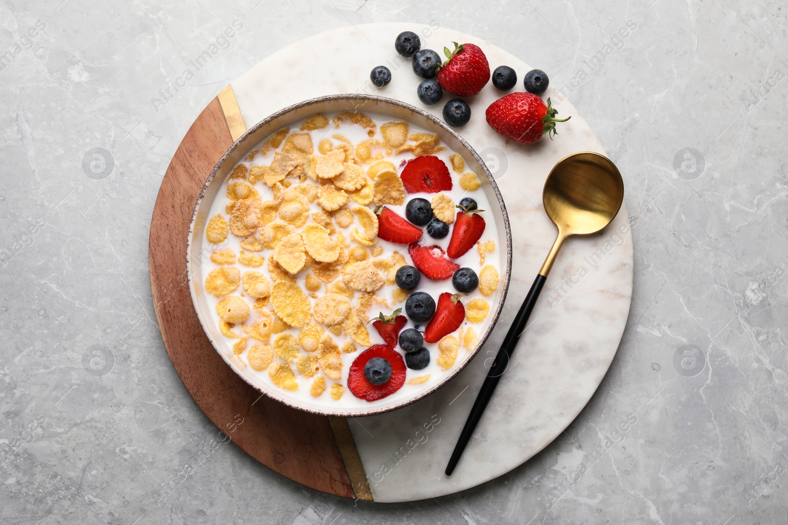 Photo of Bowl of tasty crispy corn flakes with milk and berries on light grey table, top view