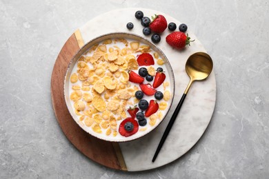 Photo of Bowl of tasty crispy corn flakes with milk and berries on light grey table, top view