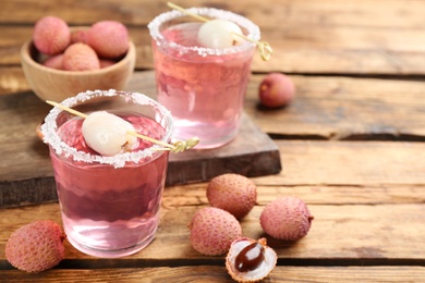 Photo of Lychee cocktail and fresh fruits on wooden table, space for text