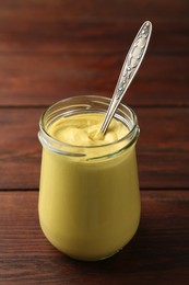 Photo of Tasty mustard sauce and spoon in glass jar on wooden table