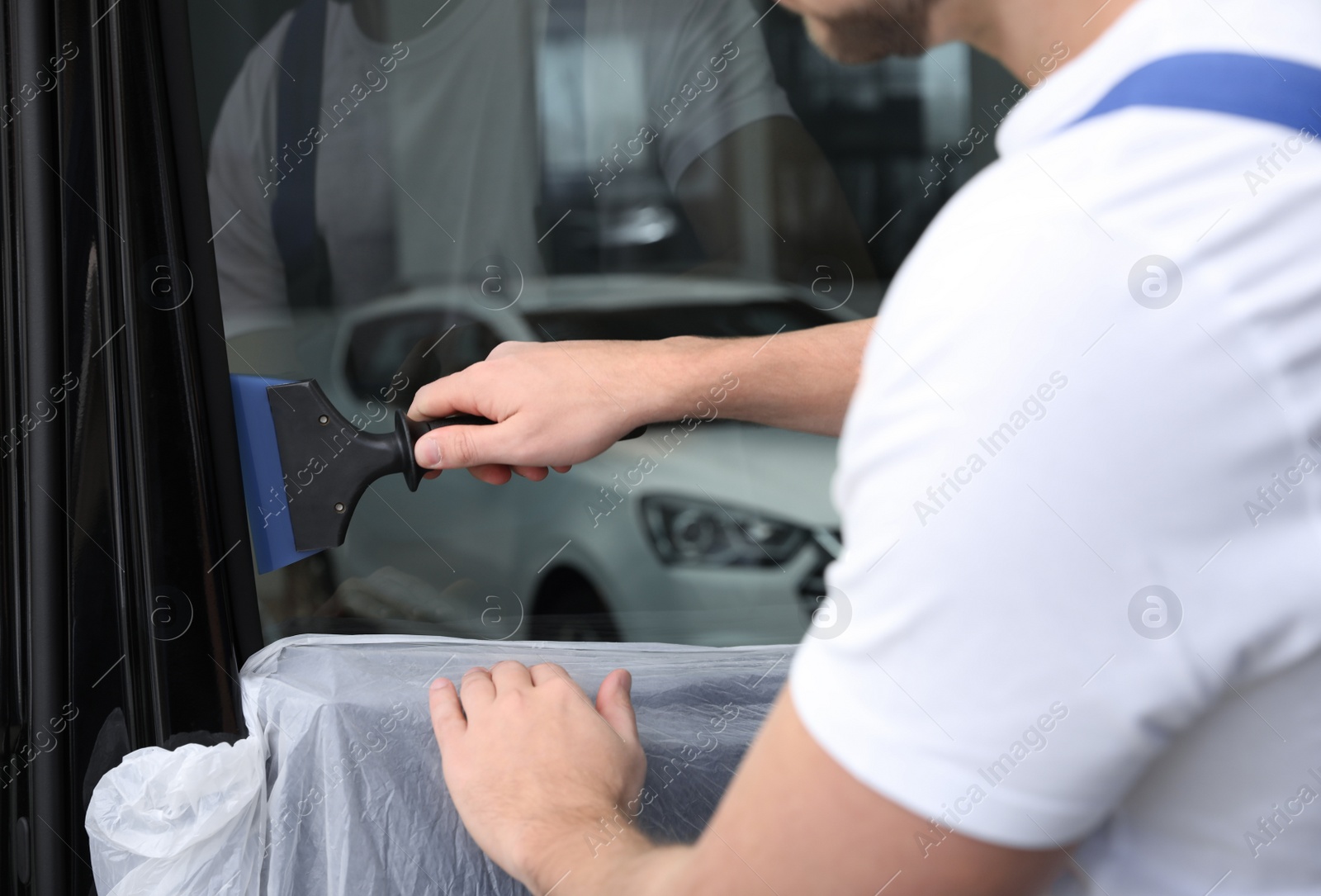 Photo of Worker tinting car window with foil in workshop, closeup