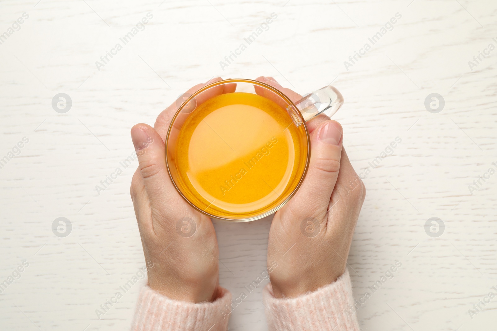 Photo of Woman with cup of fresh sea buckthorn tea at white wooden table, top view