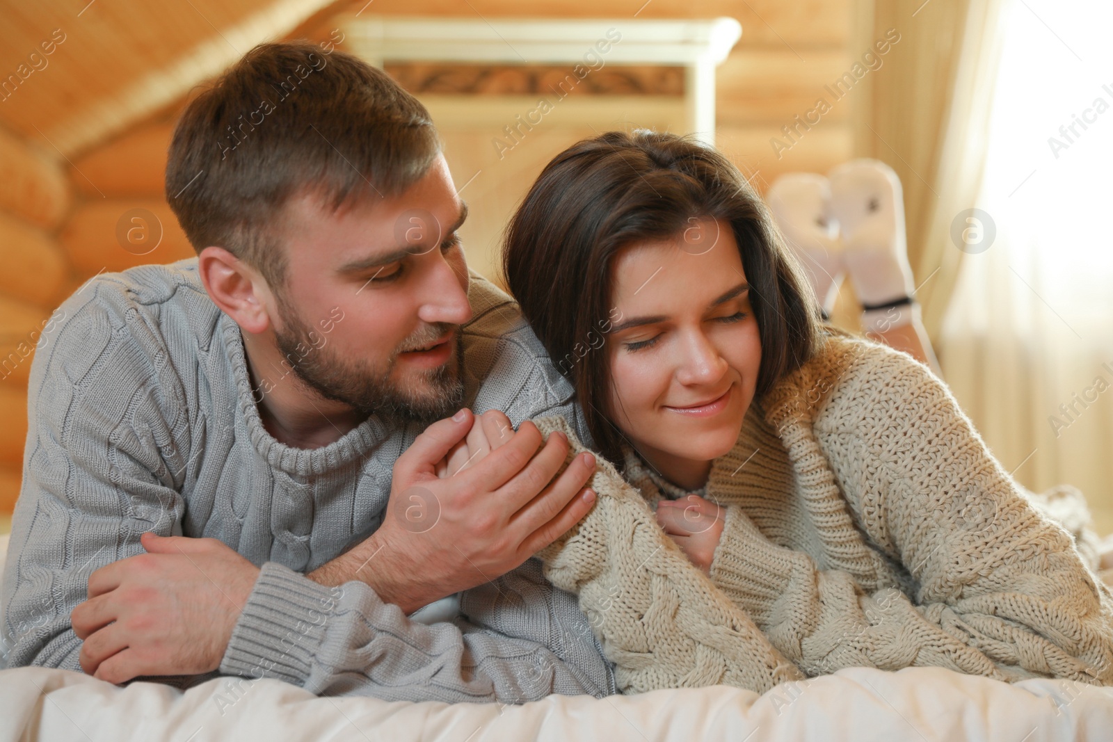 Photo of Young couple wearing warm sweaters on bed at home