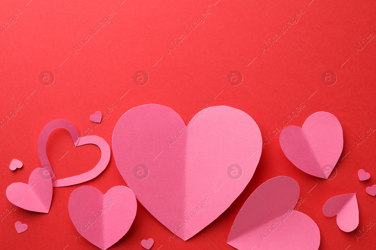 Photo of Pink paper hearts on red background, flat lay. Space for text