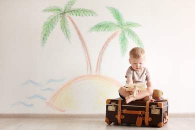 Adorable little child playing traveler with suitcase indoors