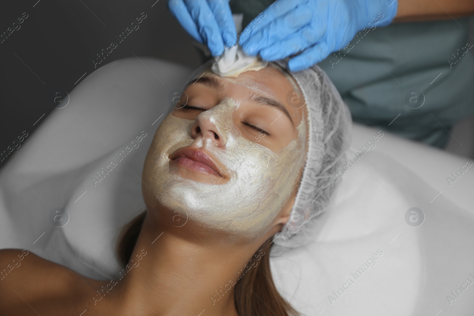 Photo of Cosmetologist removing mask from client's face in spa salon