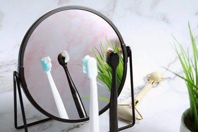 Photo of Toothbrushes with paste, mirror and facial roller on white marble table