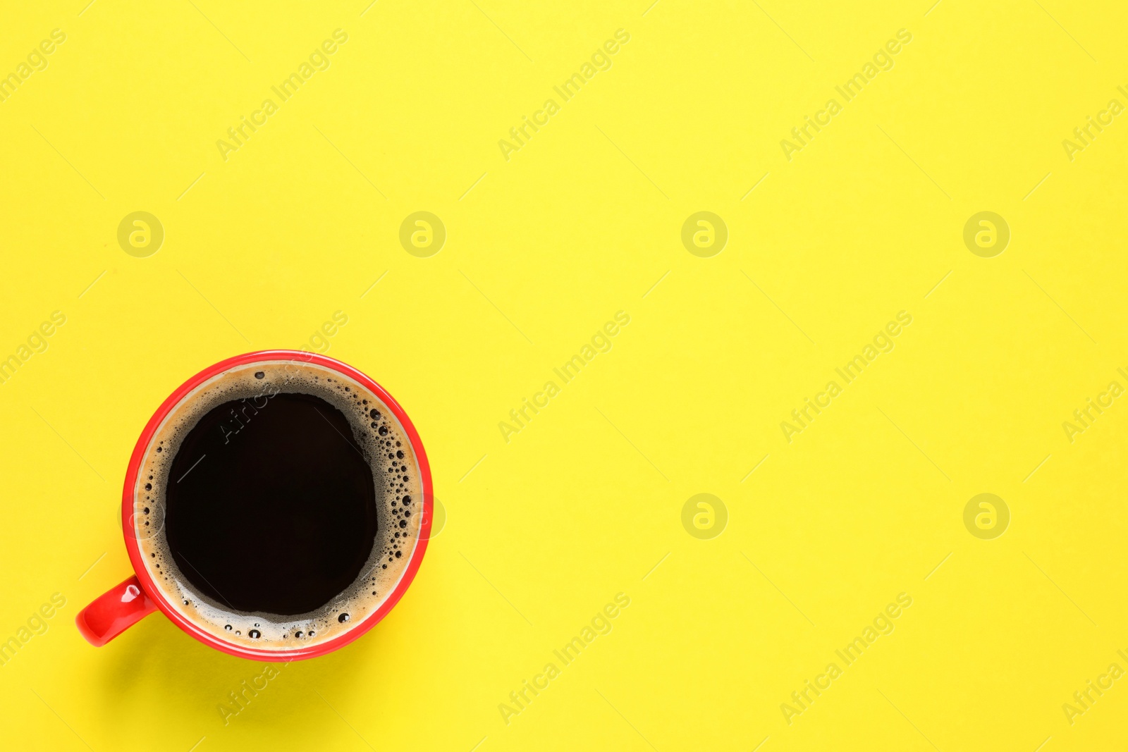 Photo of Aromatic coffee in red cup on yellow background, top view. Space for text