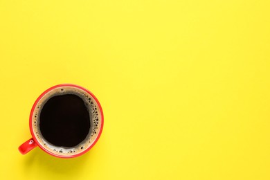 Photo of Aromatic coffee in red cup on yellow background, top view. Space for text