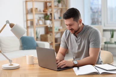 Happy man working on laptop at wooden desk in room