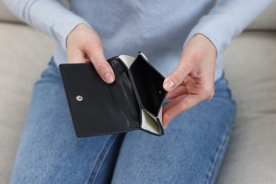 Woman with empty wallet on sofa indoors, closeup