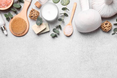 Flat lay composition with herbal massage bags, spa products and eucalyptus branches on light grey table. Space for text