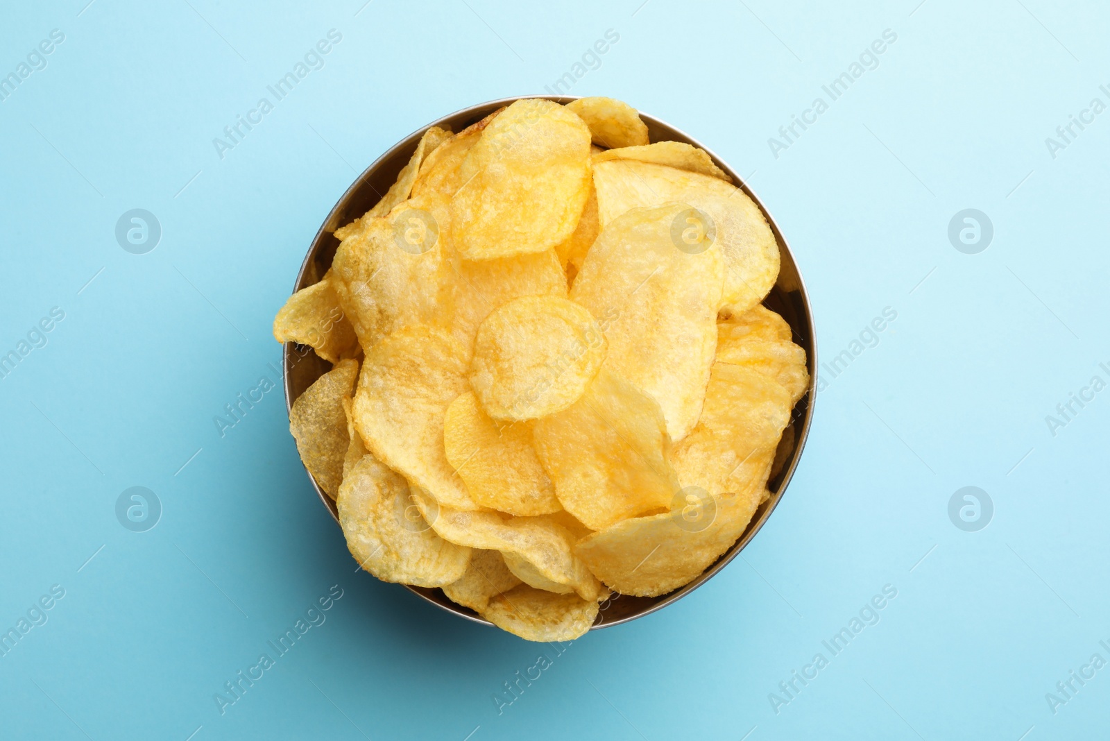 Photo of Delicious crispy potato chips in bowl on color background, top view