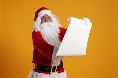 Photo of Merry Christmas. Santa Claus reading wishlist on orange background