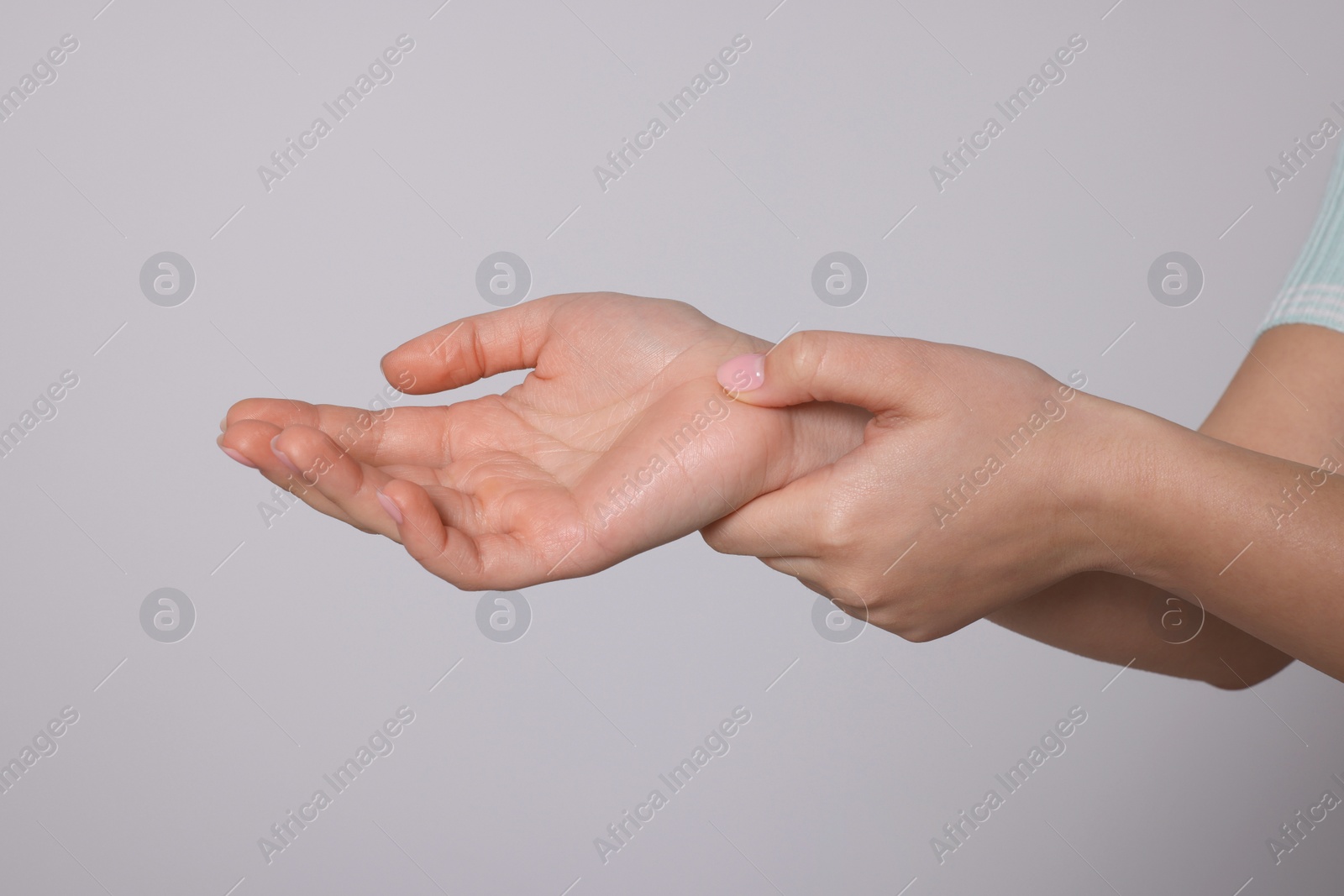 Photo of Young woman suffering from pain in hands on light grey background, closeup. Arthritis symptoms