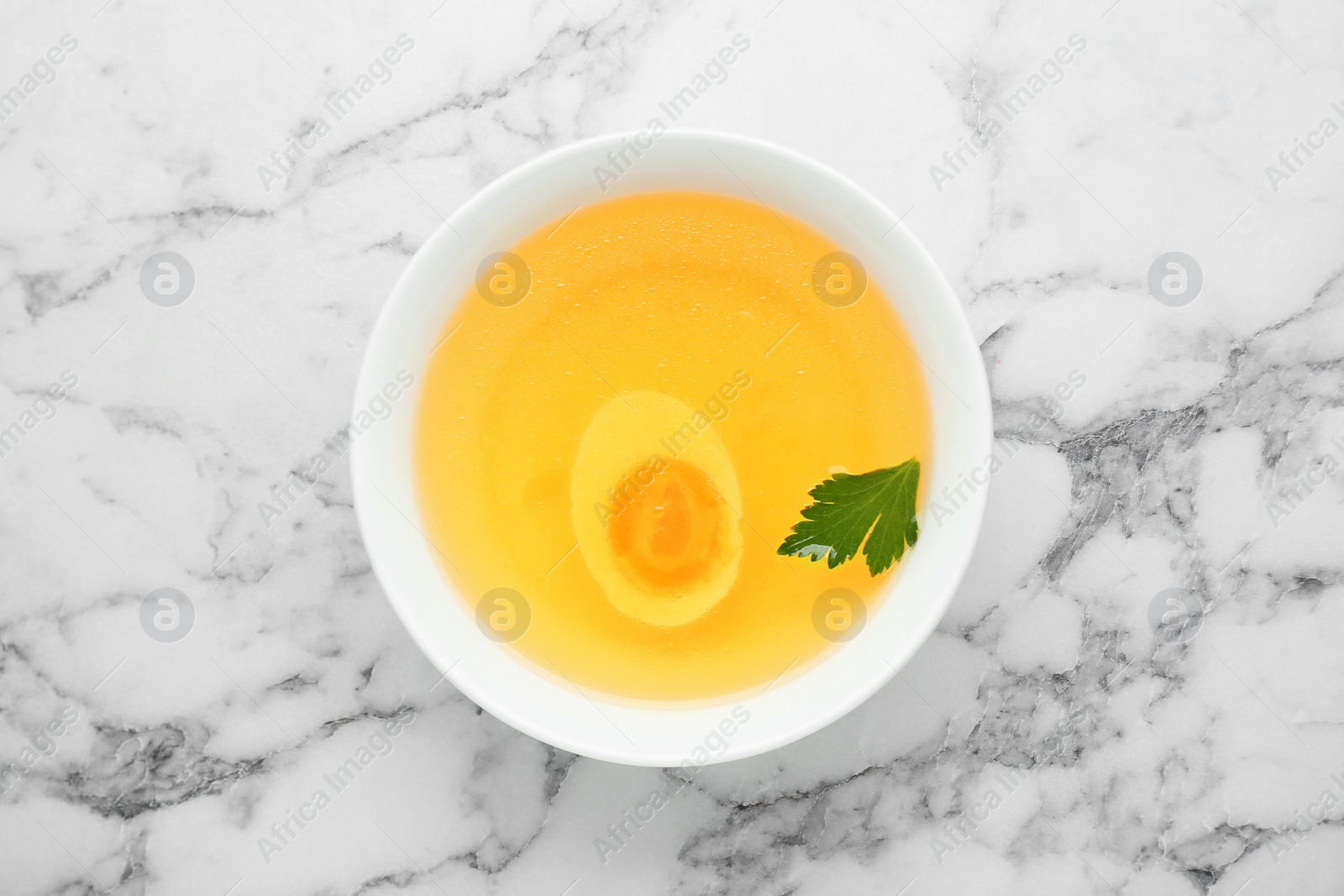 Photo of Delicious bouillon with egg and parsley in bowl on white marble table, top view