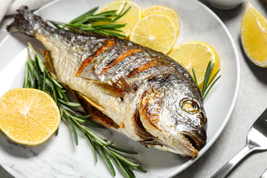 Photo of Delicious roasted fish with lemon and greens on plate, closeup