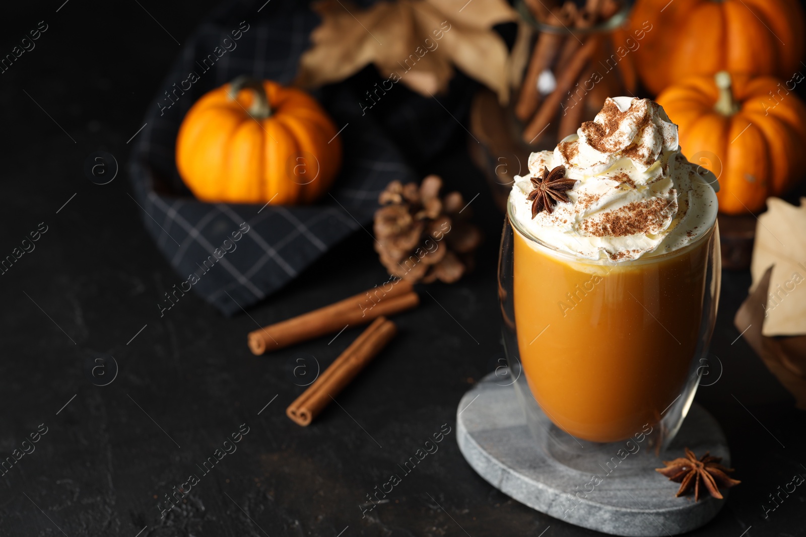 Photo of Glass of pumpkin spice latte with whipped cream and ingredients on black table. Space for text