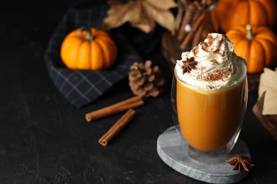 Glass of pumpkin spice latte with whipped cream and ingredients on black table. Space for text