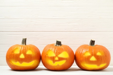 Photo of Scary jack o'lantern pumpkins on white wooden background, space for text. Halloween decor