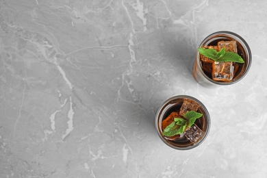 Glasses of refreshing soda drink with ice cubes and mint on grey table, flat lay. Space for text