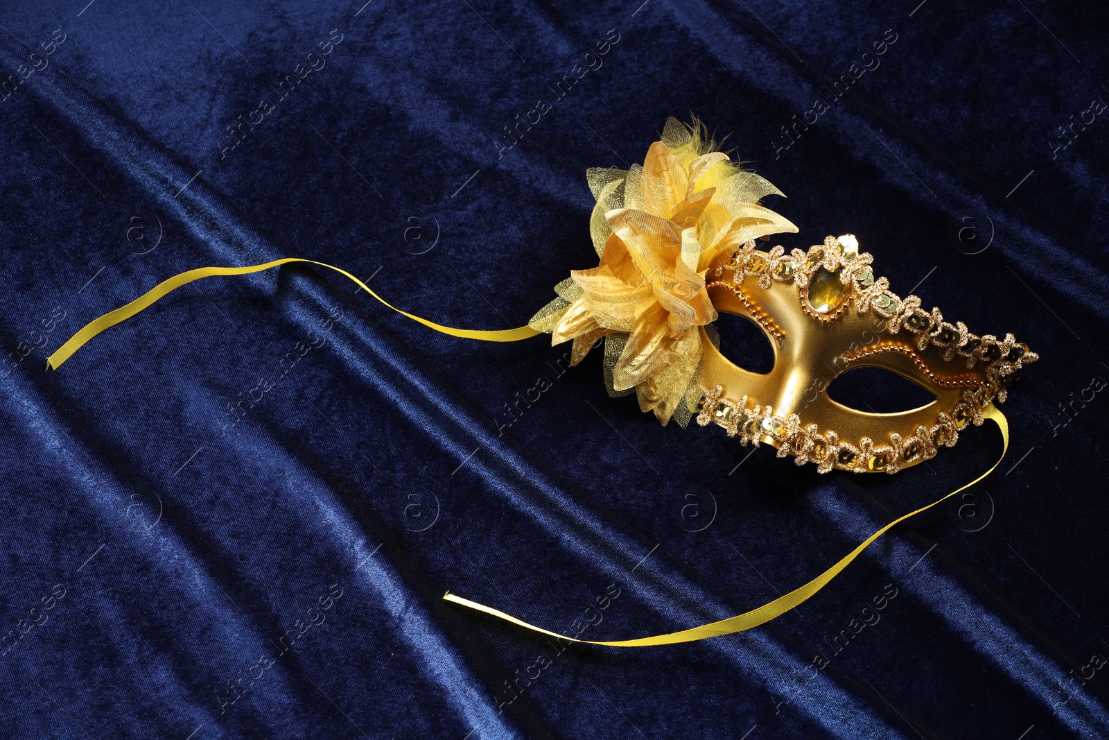 Photo of Theater arts. Golden venetian carnival mask on blue fabric, top view