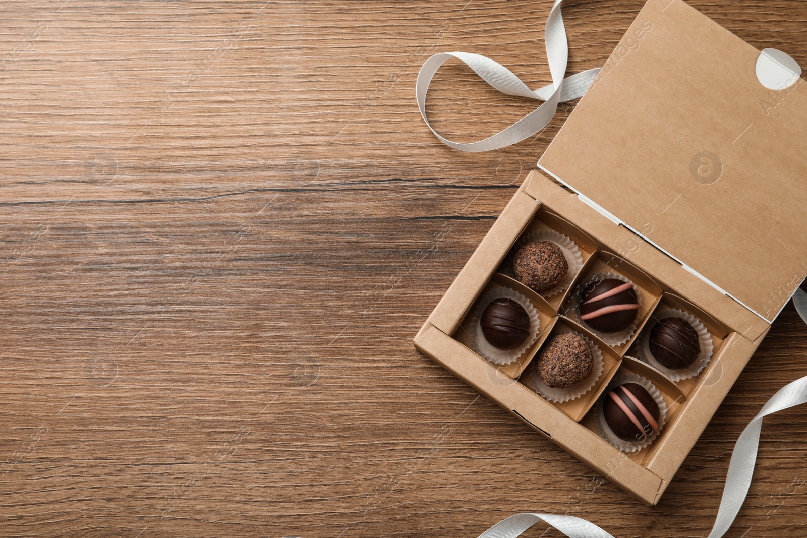 Photo of Box with many different delicious chocolate truffles on wooden table, top view. Space for text