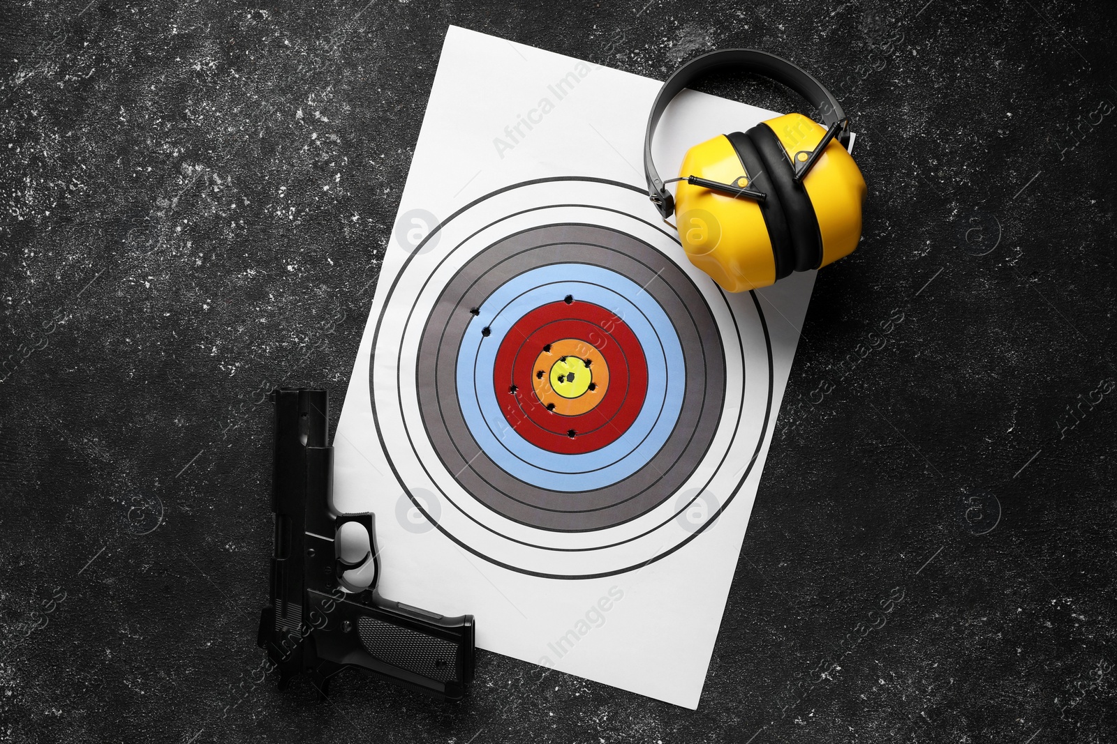 Photo of Shooting target, handgun and headphones on dark gray table, top view