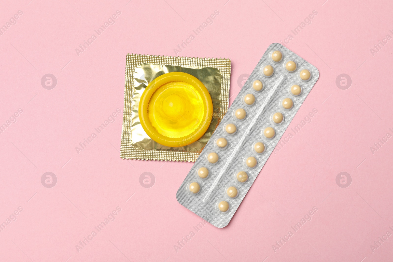 Photo of Condoms and birth control pills on pink background, top view. Safe sex