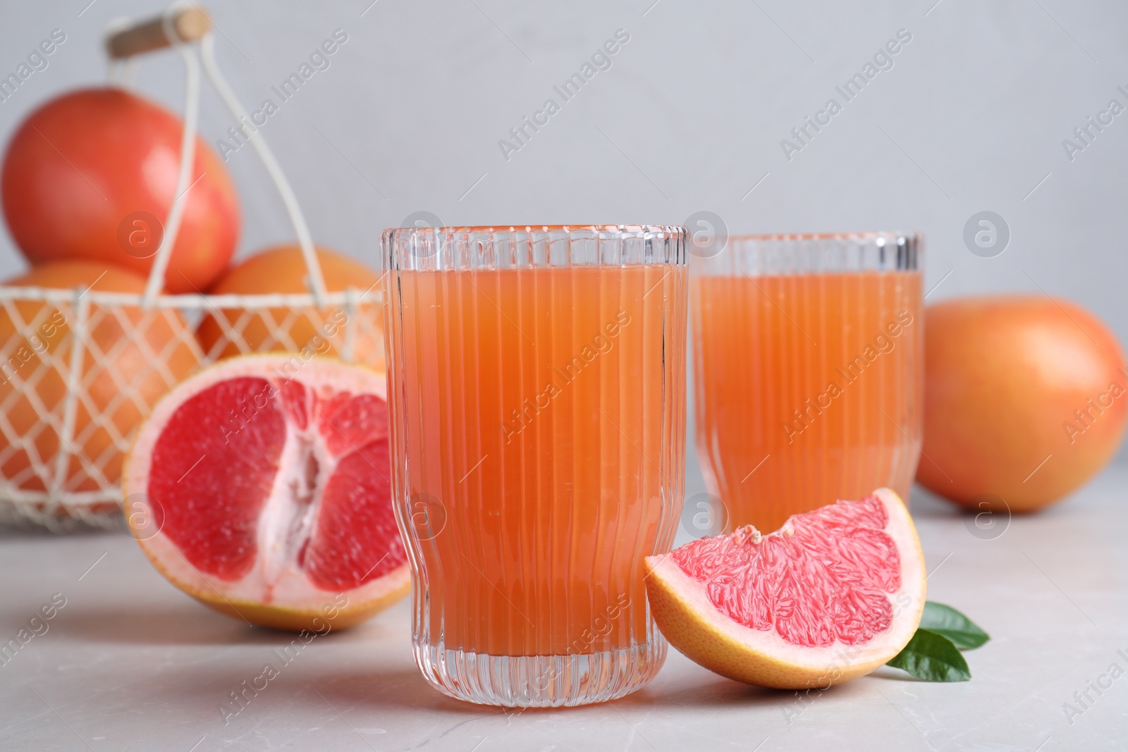 Photo of Tasty freshly made grapefruit juice and fruit on light grey marble table