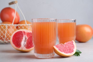 Photo of Tasty freshly made grapefruit juice and fruit on light grey marble table