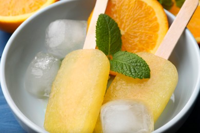 Photo of Tasty orange ice pops in bowl on table, closeup. Fruit popsicle