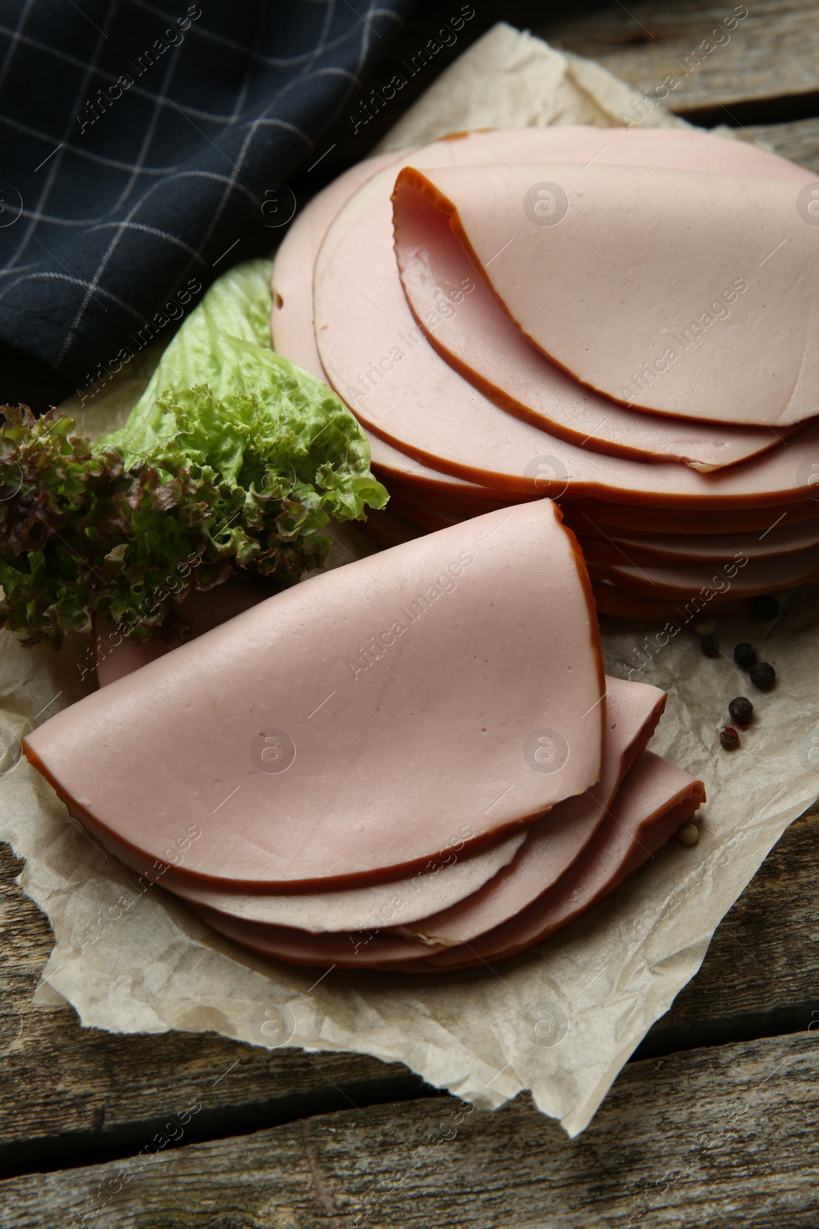 Photo of Slices of delicious boiled sausage with lettuce and spices on wooden table, above view