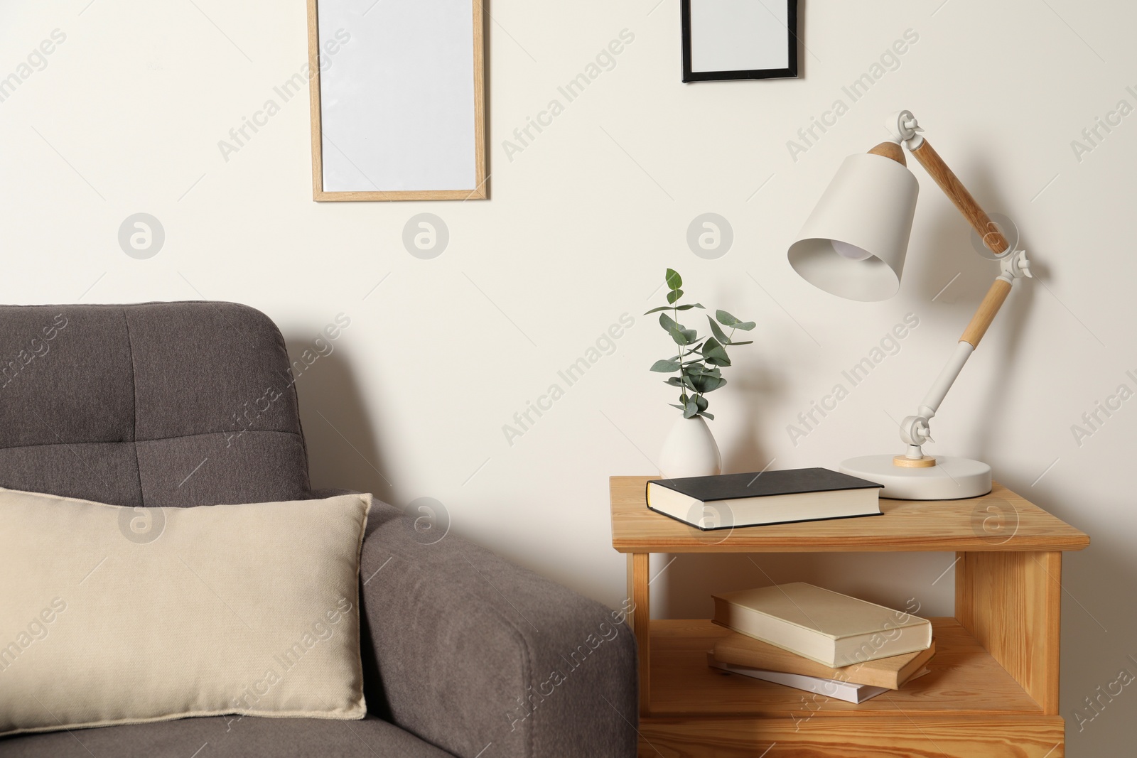 Photo of Stylish modern desk lamp, book and plant on wooden cabinet near white wall indoors