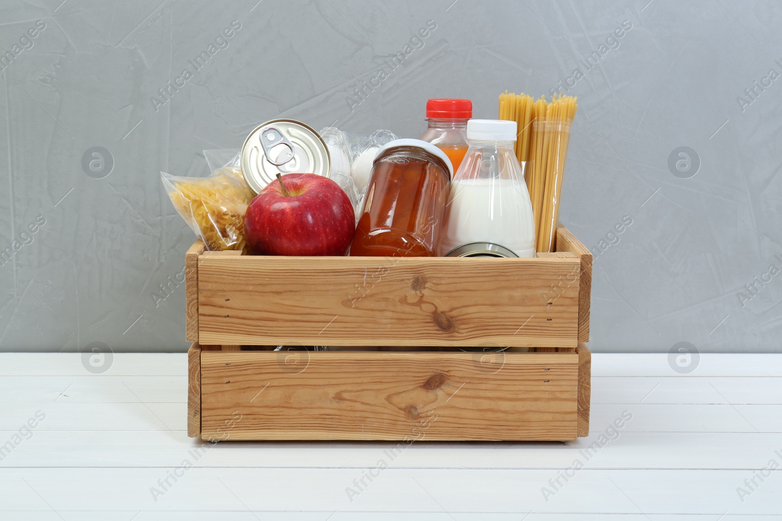 Photo of Humanitarian aid. Different food products for donation in crate on white wooden table