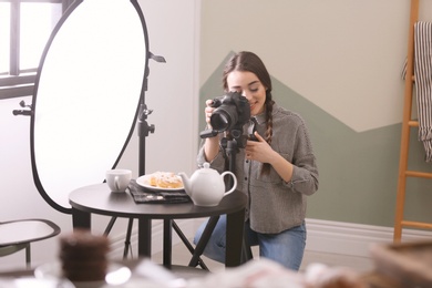 Young woman with professional camera taking food photo in studio