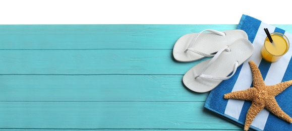 Photo of Towel, shoes, drink and starfish on light blue wooden table, space for text. Beach accessories