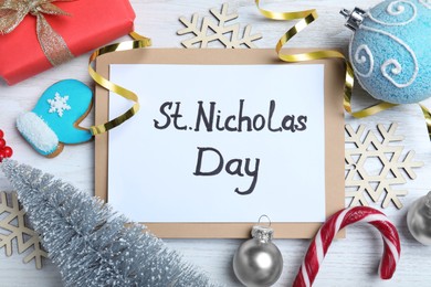 Photo of Card with text St. Nicholas Day and festive decor on white wooden table, flat lay