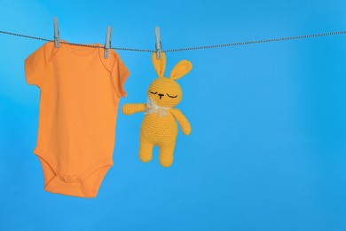 Photo of Baby onesie and bunny toy drying on laundry line against light blue background, space for text