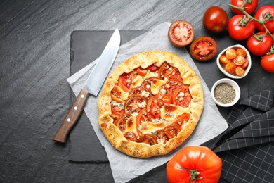 Photo of Flat lay composition of tasty galette with tomato and cheese (Caprese galette) on dark textured table. Space for text