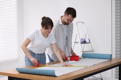 Photo of Woman and man applying glue onto wallpaper sheet at wooden table indoors