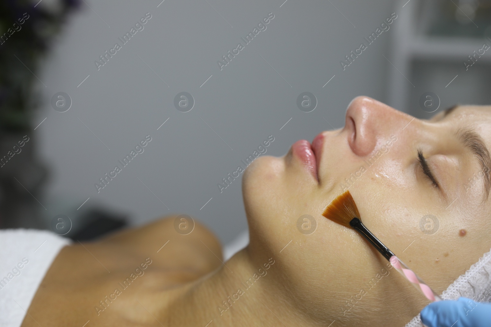 Photo of Cosmetologist applying cosmetic product for chemical peeling on client's face in salon, closeup