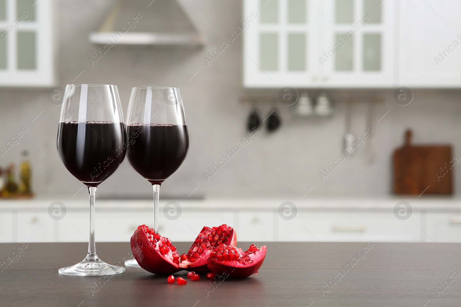 Photo of Glasses of red wine and fresh pomegranate on countertop in kitchen, space for text