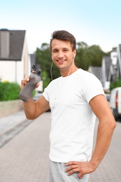 Young man with earphones drinking water after running on street. Healthy lifestyle