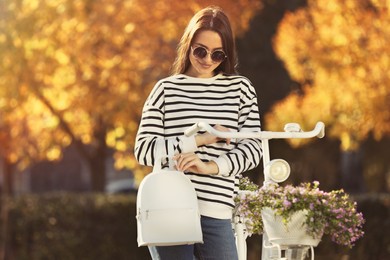 Young woman with stylish backpack and bicycle on autumn day