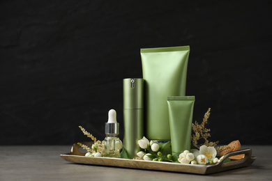 Photo of Set of cosmetic products and flowers on grey table against black background
